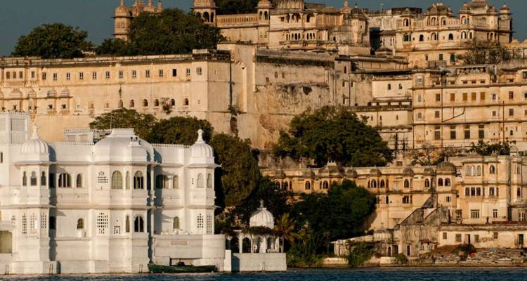 Les façades palatiales dorées d'Udaipur s'élèvent au-dessus du lac Pichola avec un palais insulaire blanc au premier plan.