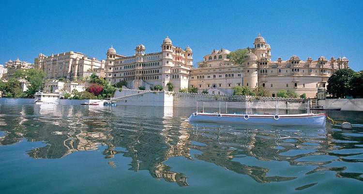 Le vaste complexe du City Palace se reflète dans les eaux bleues calmes du lac Pichola sous un ciel dégagé.