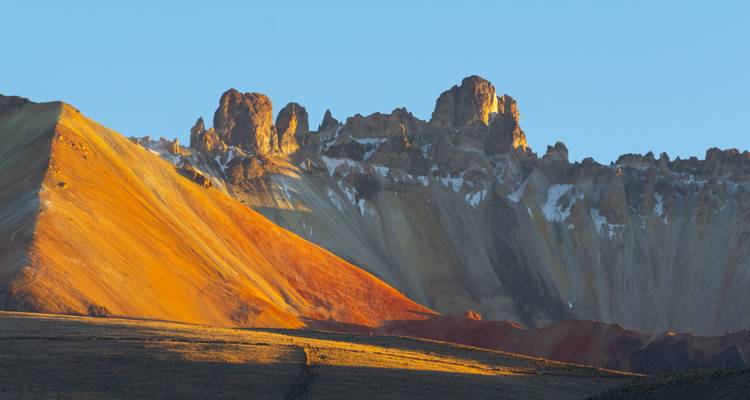 Kleurrijke vulkanische bergkam die oranje gloeit in het lage zonlicht tegen een heldere hemel in de Altiplano.