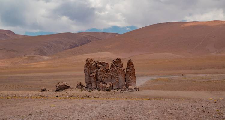 Geïsoleerde verticale rotsformaties die oprijzen uit een kaal roodachtig plateau onder gedeeltelijk bewolkte luchten.