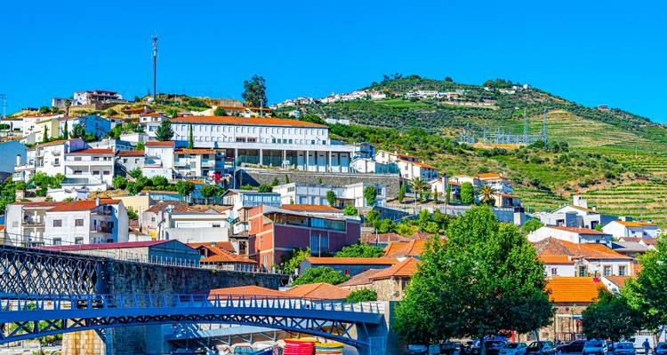 Bright hillside town with whitewashed and terracotta houses above a riverside bridge on a clear blue-sky day.