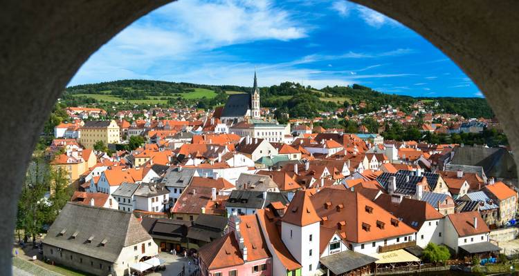Picturesque red-roofed town sprawls across rolling hills, framed by a stone arch viewpoint.