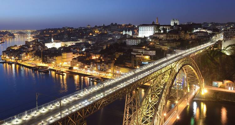Puente Dom Luís I iluminado sobre el río Douro y las luces de la ciudad de Oporto después del anochecer.