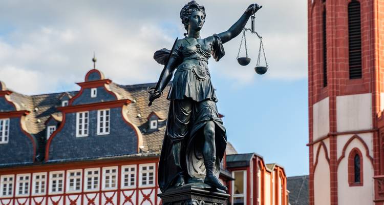 Statue de Dame Justice tenant une balance avec des bâtiments à colombages en arrière-plan.