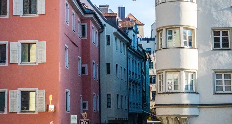 Narrow European street lined with pastel buildings and shuttered windows lit by soft morning light.