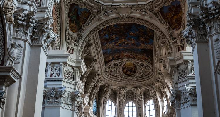 Intricately carved baroque interior of a cathedral with frescoed ceiling and ornate columns bathed in low light.