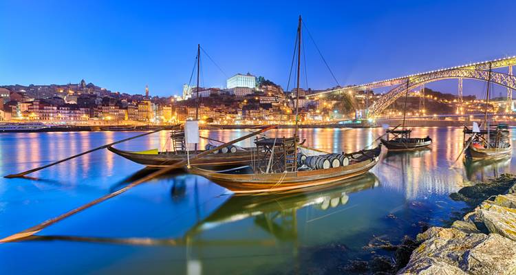 Traditional rabelo boats moored on the Douro River with Porto’s hillside lights and Dom Luís I Bridge glowing at blue hour.