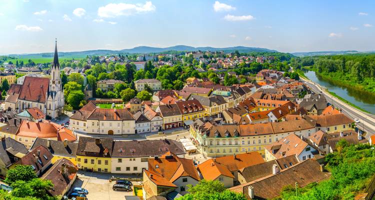 Aerial view of a quaint Austrian market town with church spire, red roofs and surrounding greenery.