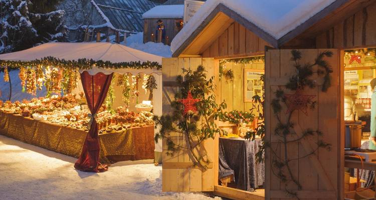 Chaleureuses échoppes de marché de Noël sous la neige avec des lumières décoratives chaleureuses et des guirlandes festives.