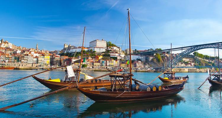 Traditional rabelo boats moored on the Douro River with Porto’s colorful skyline and Dom Luís I Bridge.