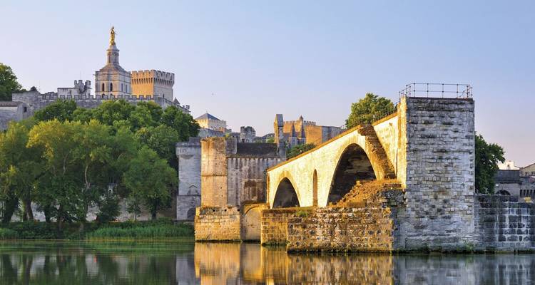 Pont de pierre médiéval enjambant le Rhône avec les remparts historiques d'Avignon et l'horizon illuminés par la douce lumière du soir.