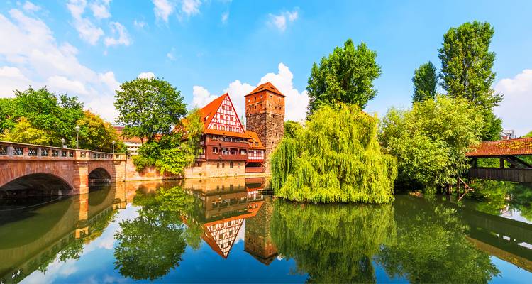 Les tours médiévales pittoresques et les maisons à colombages de Nuremberg se reflètent dans une rivière calme bordée d'arbres luxuriants.