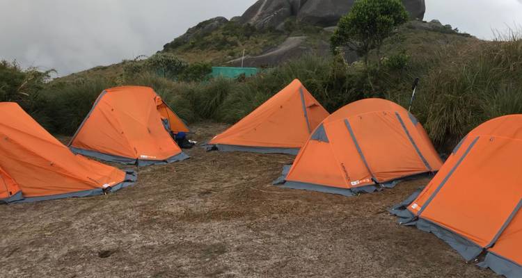 Groupe de tentes dômes orange vif installées sur un terrain de camping de montagne sec avec un arrière-plan rocheux