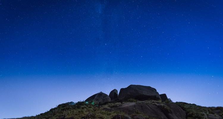 Ciel nocturne étoilé au-dessus de rochers en silhouette et lueur d'horizon faible dans les montagnes isolées