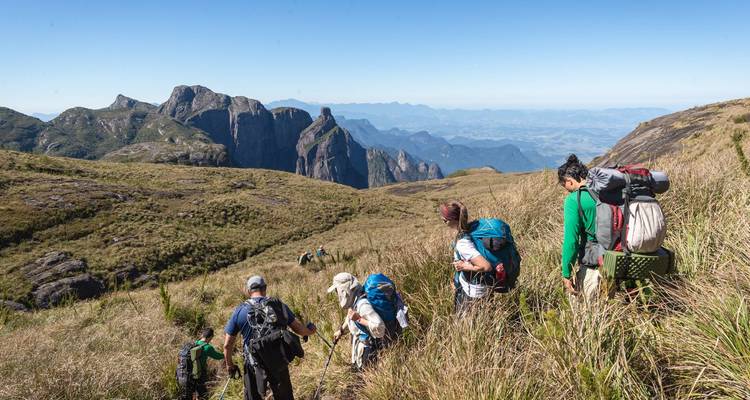 Des randonneurs avec des sacs à dos marchent à travers les hautes herbes vers des pinacles rocheux spectaculaires sous un ciel lumineux