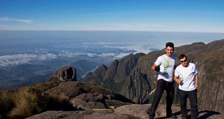 Deux randonneurs posent sur un point de vue rocheux dominant des vallées remplies de nuages et des pics escarpés