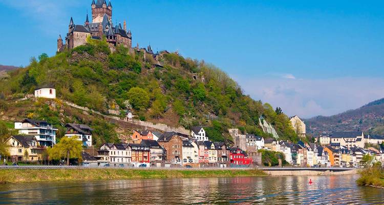 Pittoresk uitzicht op kasteel Cochem bovenop een met wijnranken bedekte heuvel met uitzicht op kleurrijke huizen aan de rivier.