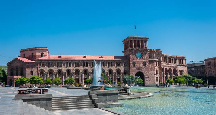 Edificio gubernamental y torre del reloj en la Plaza de la República, Ereván, con fuentes centrales y cielo azul brillante.