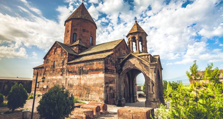 Komplexe armenischer Steinkirche mit Kegeldächern unter teilweise bewölktem Himmel.