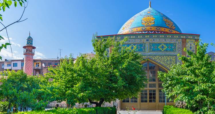 Farbenfrohe, mit Kacheln verkleidete Blaue Moschee mit Kuppeldach, umgeben von grünen Bäumen an einem sonnigen Tag.