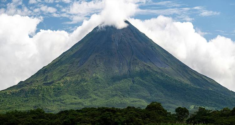 Konischer Vulkan Arenal, der sich über dem Regenwald erhebt, mit weißen Wolken, die an seinem Gipfel hängen