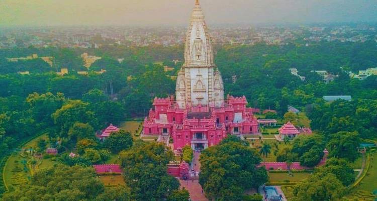 Farbenfrohe Luftaufnahme eines großen rosa Hindu-Tempelkomplexes umgeben von dichtem Grün und Stadtlandschaft