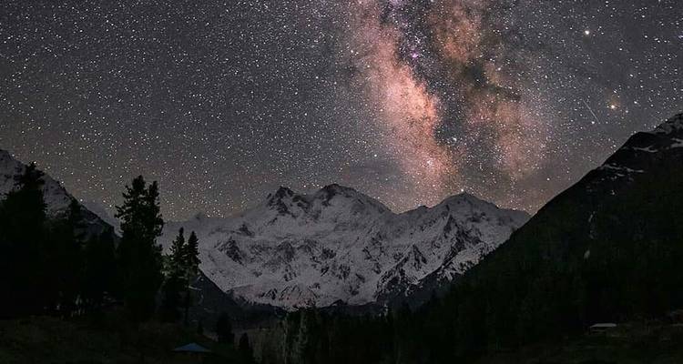Milky Way shining over snowy mountain silhouette at night in Fairy Meadows