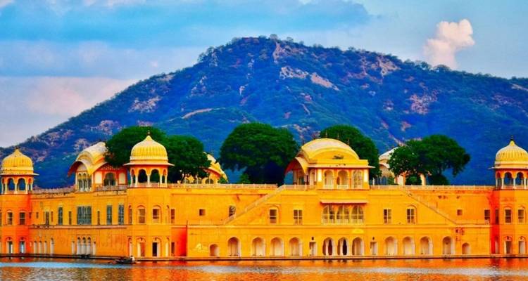 Goldener Jal Mahal Palast, der auf einem ruhigen See mit bewaldetem Hügel im Hintergrund schwimmt.