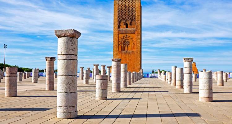 Rows of marble columns lead to the red-brick Hassan Tower under a blue sky in Rabat.