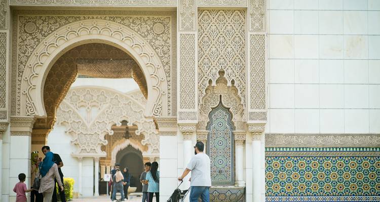 Intricately carved archways of the Hassan II Mosque frame visitors walking beneath patterned stonework in Casablanca.