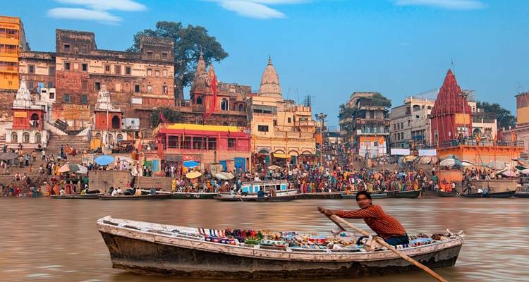 Bootsman roeiend voor de kleurrijke ghats en tempels langs de rivier de Ganges.