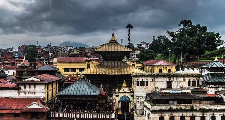 Complejo de templos histórico con techo dorado contra dramáticas nubes de tormenta sobre el bullicioso paisaje urbano de Katmandú.