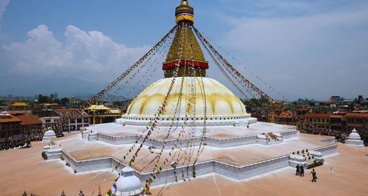 Gran estupa blanca adornada con banderas de oración coloridas que domina un amplio patio con montañas brumosas a la distancia.