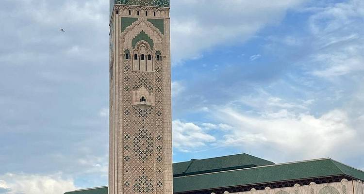 Hoher Minarett und Fassade der Hassan-II-Moschee vor einem teilweise bewölkten Küstenhimmel in Casablanca.