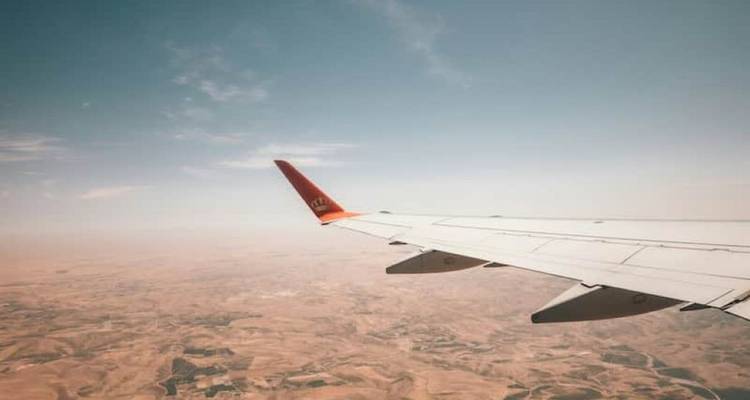 Aile d'avion au-dessus d'un paysage désertique aride sous un ciel bleu pâle vue depuis un siège près du hublot.
