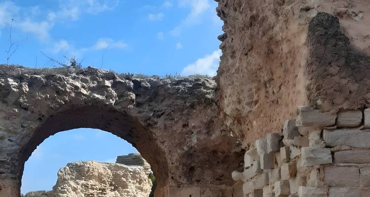 Dichtbij zicht van een stenen boog en afbrokkelende muur van oude ruïnes onder een blauwe hemel.