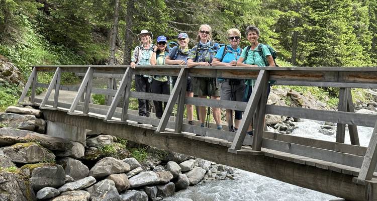 Grupo de senderistas se apoya en un puente de madera sobre un arroyo alpino rugiente rodeado de bosque.
