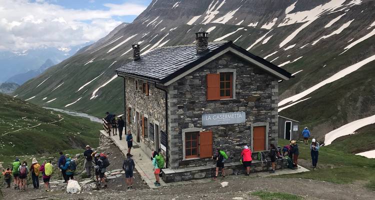 Gran grupo de excursionistas se reúne fuera del refugio de montaña de piedra 'La Casermetta' entre picos nevados.