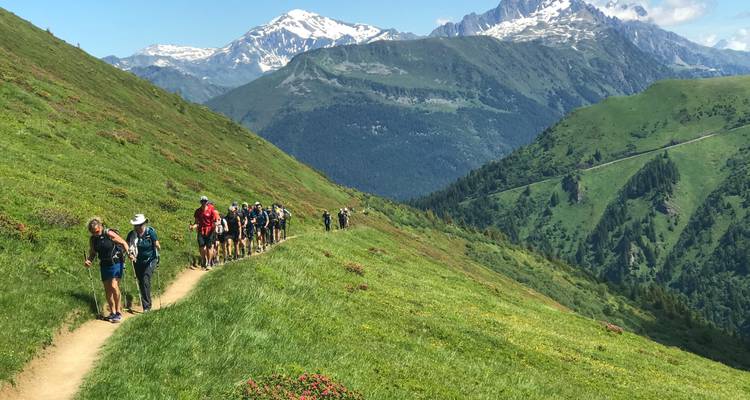 Fila de excursionistas sigue un sendero de cresta cubierto de hierba con vistas panorámicas de montañas por todas partes.