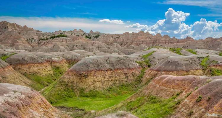 Collines érodées aux bandes colorées et formations dentelées du parc national des Badlands sous un ciel bleu.