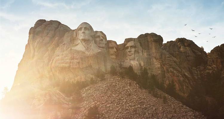 Sculptures iconiques du Mont Rushmore éclairées par un lever de soleil chaleureux avec des oiseaux planant au-dessus.