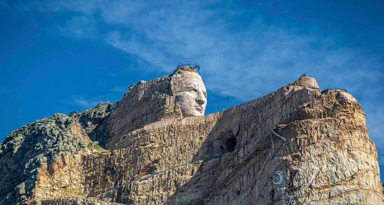 Monument en granit du Mémorial de Crazy Horse émergeant d'une falaise escarpée contre un ciel bleu profond.