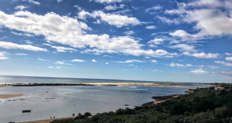Weites Küstenpanorama der Sandbänke der Algarve und des blauen Atlantischen Ozeans unter gepunkteten Wolken.