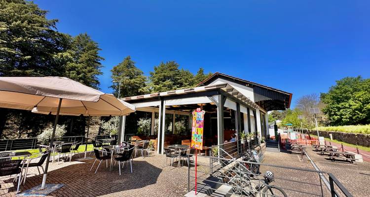 Outdoor-Terrassencafé und Fahrradständer neben einem modernen Rastplatz am Bahntrassenweg unter klarem Himmel.