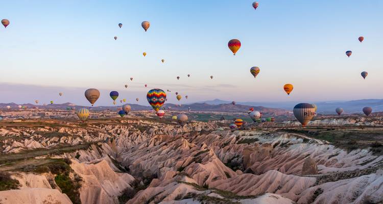 Docenas de globos aerostáticos coloridos flotan sobre los valles rosados ondulados de Capadocia al amanecer.
