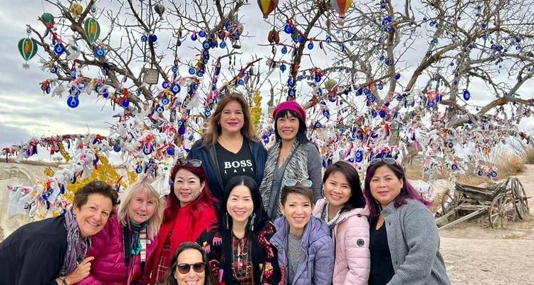 Viajeros sonrientes reunidos ante el árbol de amuletos contra el mal de ojo en el paisaje abierto de Capadocia.
