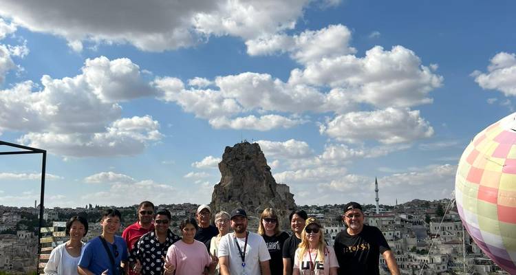 Grupo de turistas con ciudadela rocosa alzándose detrás de ellos bajo nubes dispersas.