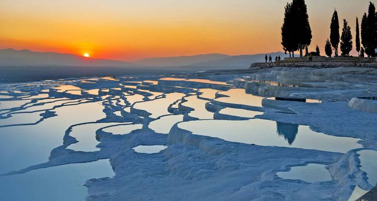 Atardecer resplandeciente sobre las terrazas blancas de travertino de Pamukkale reflejando el cielo naranja.