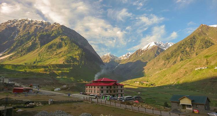 Vallée de montagne parsemée d'un hôtel au toit rouge et de champs en terrasses sous un ciel partiellement nuageux.