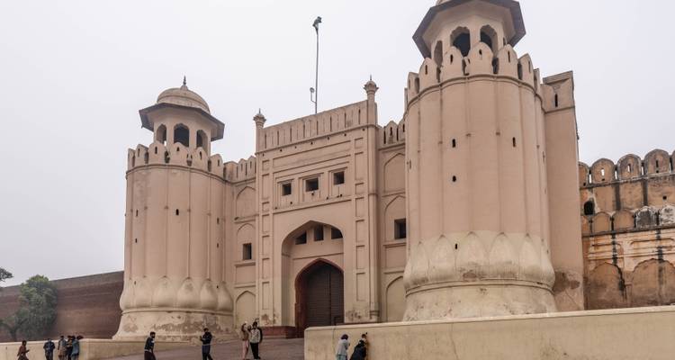 Entrée historique du Fort de Lahore avec des visiteurs traversant la cour par une journée brumeuse.